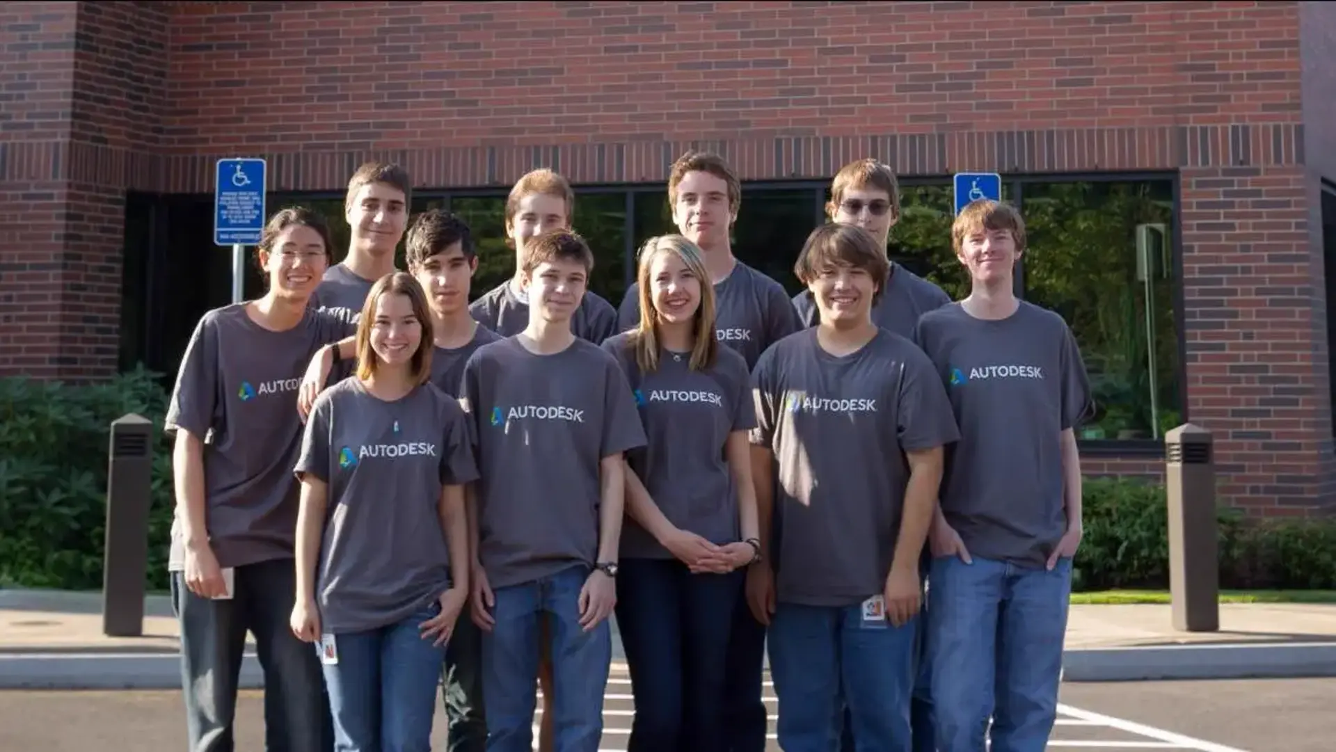 A group of 11 people standing togething looking at the camera in a parking lot, all wearing gray Autodesk t-shirts